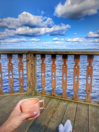 Midsection of person holding drink against water against sky