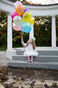 Girl holding helium balloons while sitting on steps