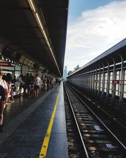 People waiting at railroad station platform against sky