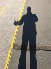 Shadow of man hitchhiking on road