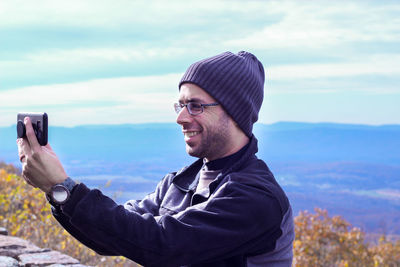 Smiling man using smart phone against sky