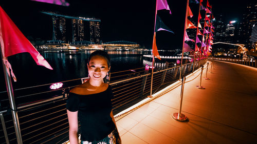 Portrait of young woman standing in illuminated city at night