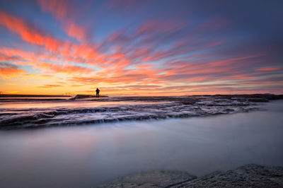 Man standing at beach against sky during sunset