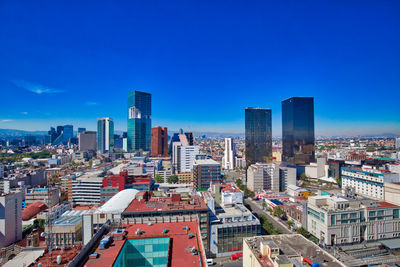 Aerial view of buildings in city against blue sky