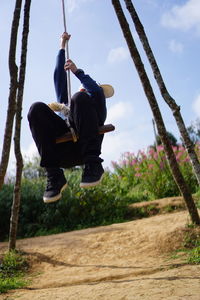 Low angle view of man enjoying on swing against sky