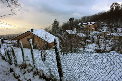 Snow covered house by building against sky