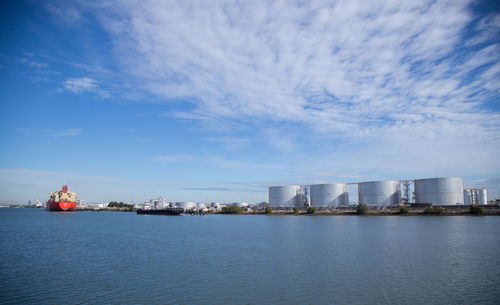 Calm sea with silos in distance against sky