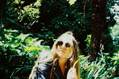 Portrait of young woman wearing sunglasses against trees