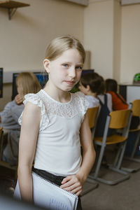 Portrait of girl holding notebook while standing in computer classroom at school