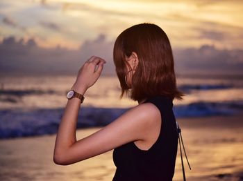 Midsection of woman standing at beach against sky during sunset