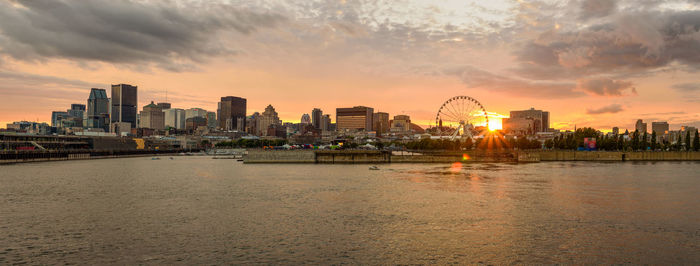 City by river against sky during sunset