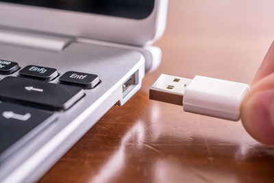 Cropped image of person holding usb cable by laptop at desk
