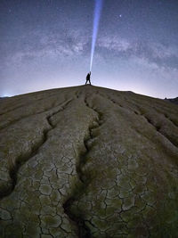 Man holding illuminated flashlight while standing on mountain against sky