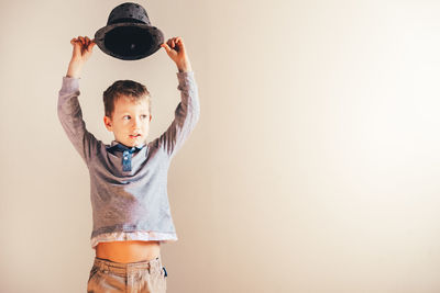 Boy holding hat against white wall