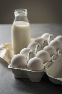 Close-up of eggs in carton with milk bottle on table