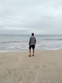 Rear view of man standing on beach against sky