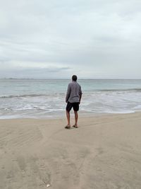 Rear view of man standing at beach against sky