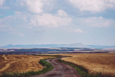 Road amidst field against sky