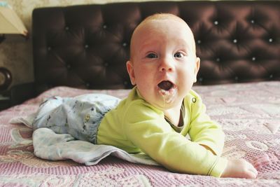 Close-up portrait of cute baby boy drooling on bed at home