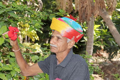 Close-up portrait an old farmer of indian origin looking at the red flower of hibiscus