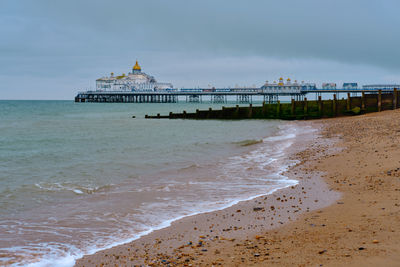 Eastbourne beach in the summer with overcast sky.  groynes and a pier in the background.