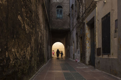 Rear view of people walking in alley amidst buildings in city