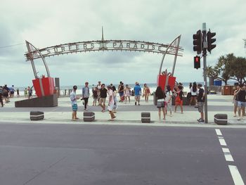 People on road by sea in city against sky