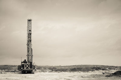 Crane on landscape against cloudy sky