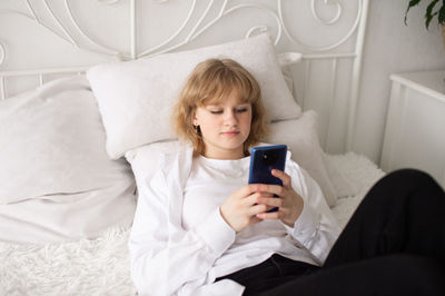 Young woman using mobile phone while lying on bed at home