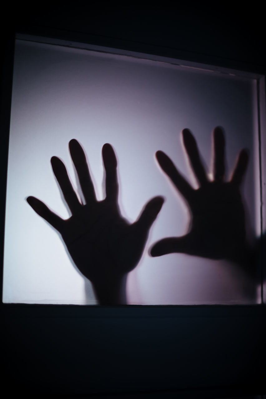 CLOSE-UP OF SILHOUETTE HAND ON GLASS