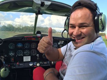 Close-up portrait of happy man gesturing thumbs up while sitting in cockpit