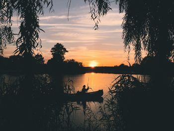 Silhouette person on lake against sky during sunset