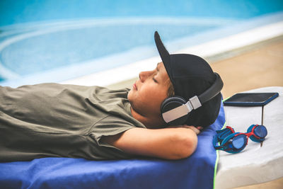 Side view of boy listening music while lying on lounge chair