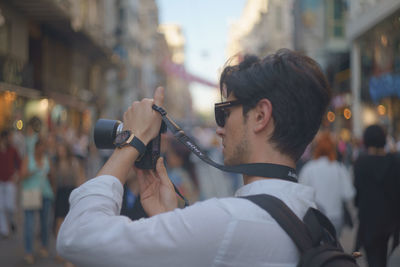 Side view of young man photographing through digital camera on street