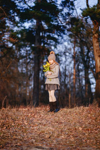 Full length of girl holding flower standing against trees