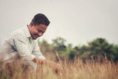 Smiling man sitting on field against sky