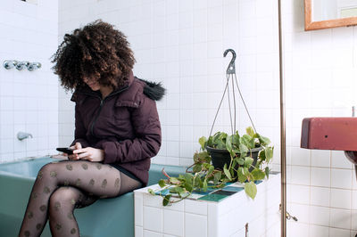 Young woman using mobile phone while sitting on bathtub