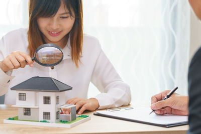 Smiling businesswoman looking at model home through magnifying glass in office