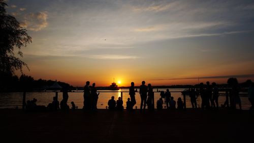 Silhouette people on beach against sky during sunset