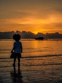 Rear view of silhouette man standing at beach during sunset