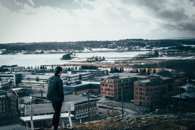 Rear view of man looking at cityscape against sky