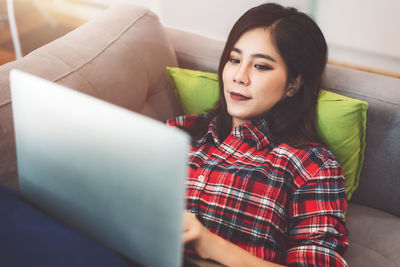 Young woman using phone while sitting on sofa at home