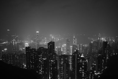 Illuminated cityscape at victoria harbour against sky