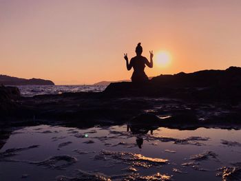 Silhouette woman showing peace sign at beach against sky during sunset