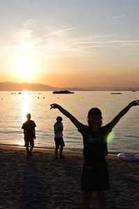 Silhouette people standing on beach against sky during sunset