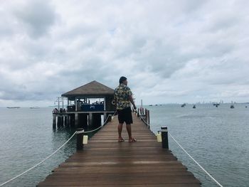 Rear view of man standing on pier over sea against sky