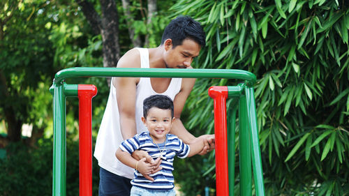 Father with smiling son against trees at playground