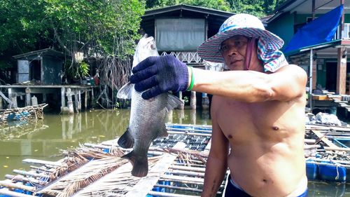 Shirtless fisherman looking at dead fish in river