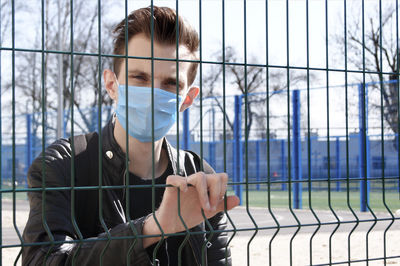 Portrait of young man standing against fence