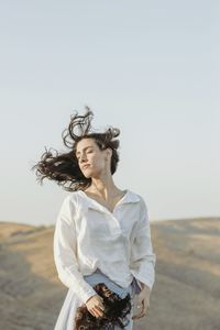 Young woman standing in front of traditional clothing against clear sky